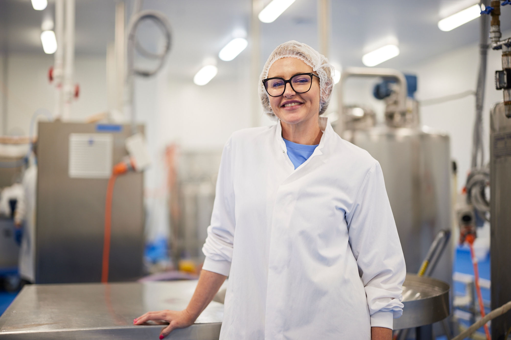 person in a hairnet smiling and a food factory behind