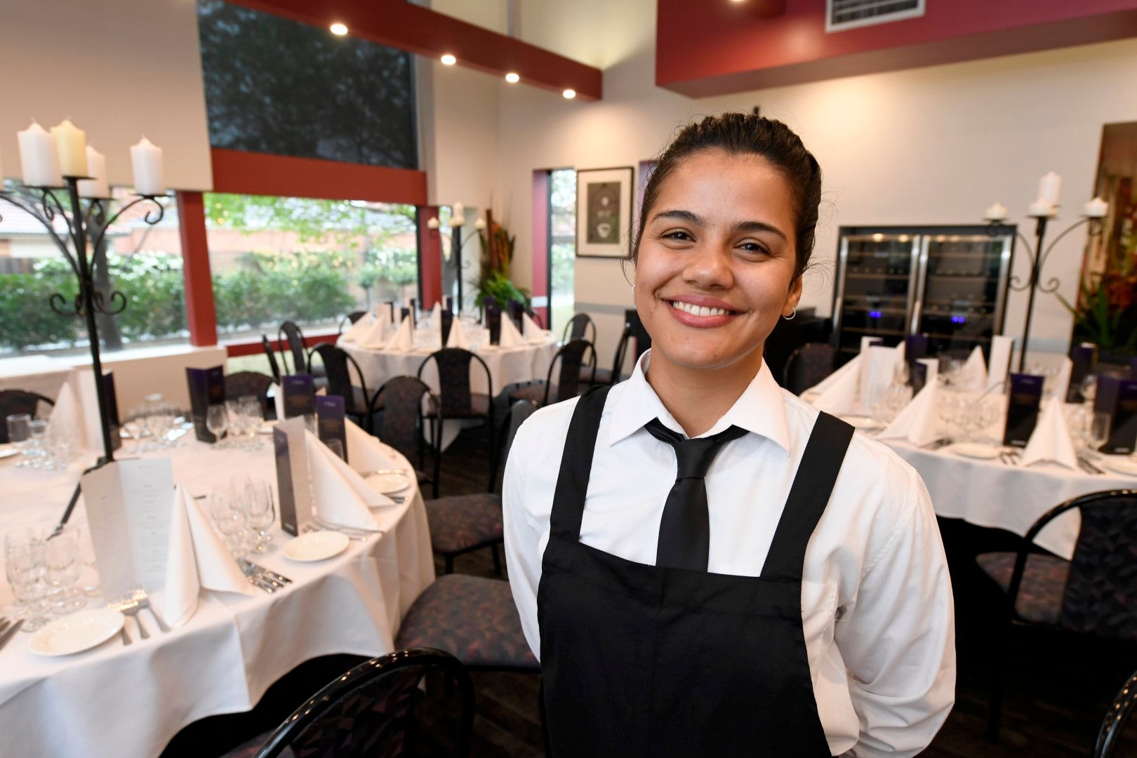 woman in black and white uniform smiling forward with cabaret tables set in background 