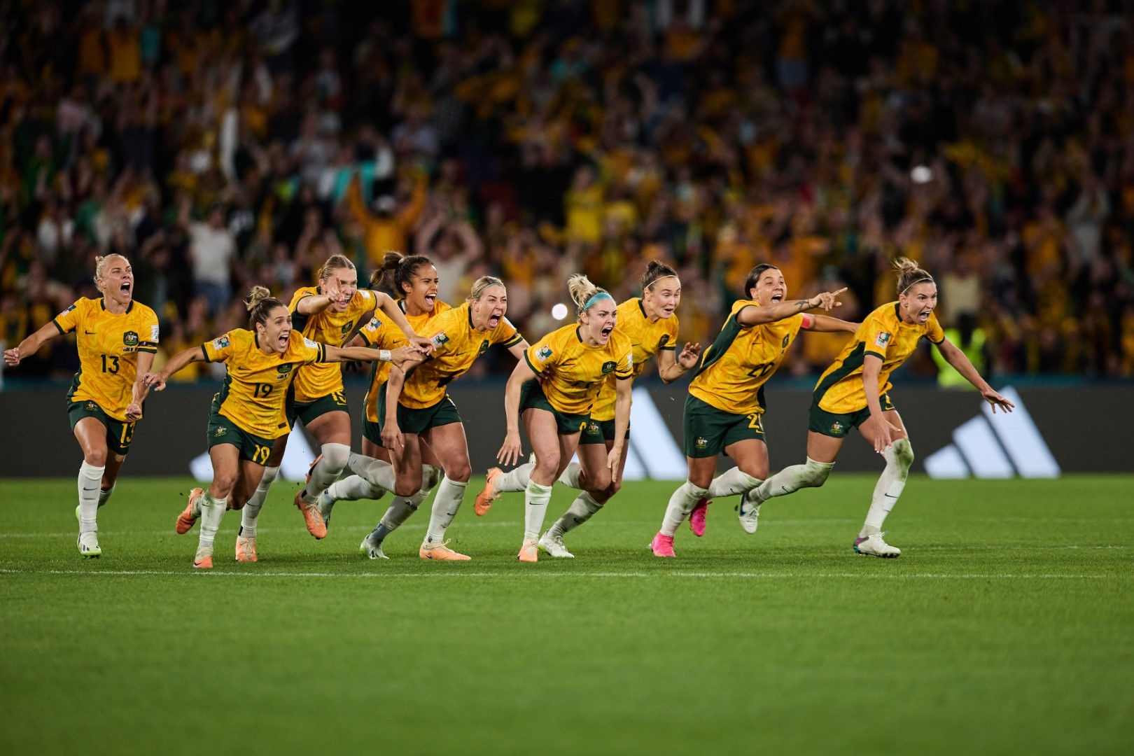 Australian womans football team in a running motion celebrating on a soccer pitch 