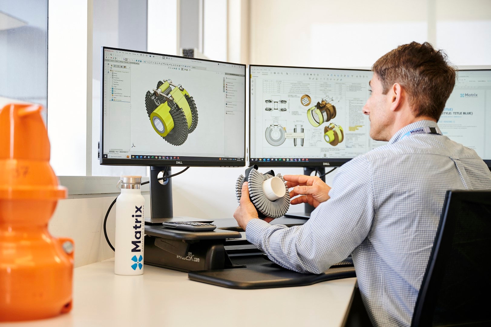 man sitting on chair facing desk with two monitors 