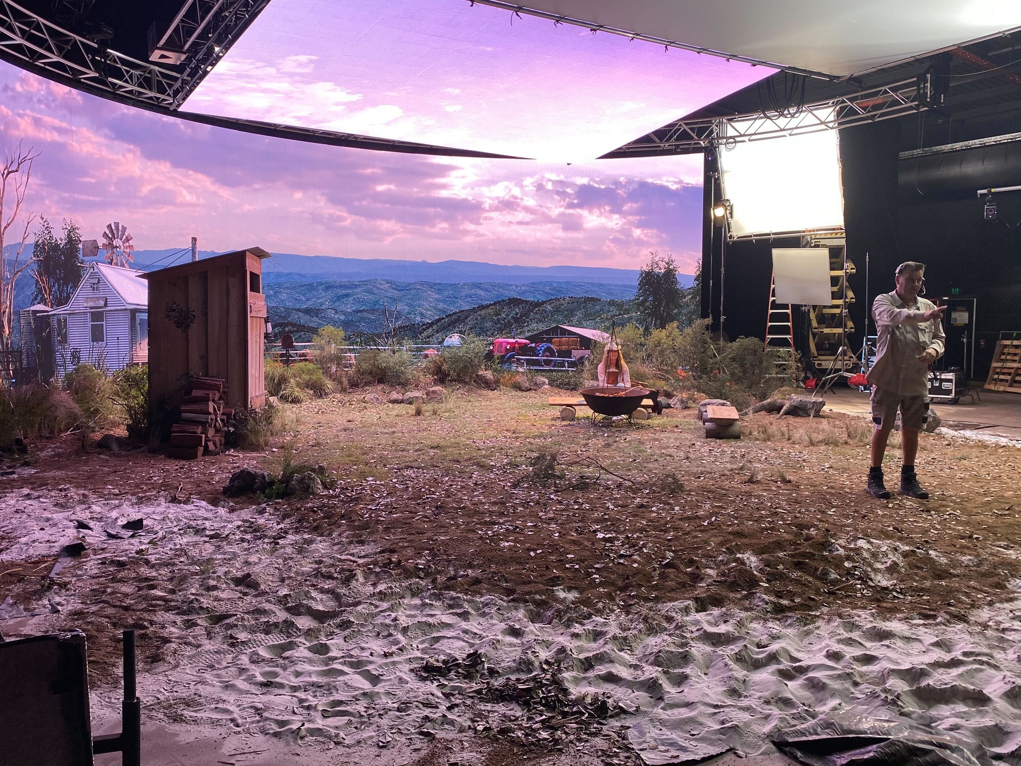 screen production of wilderness background with a white house and a outdoor toilet and a man standing.