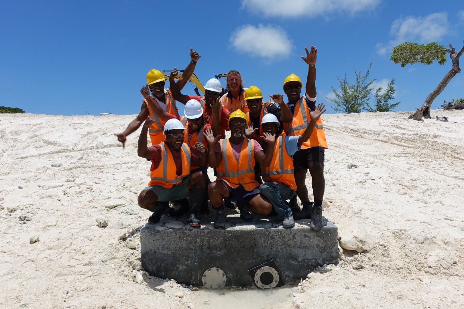 group of people on beach in orange high vis and yellow and white hard hats 