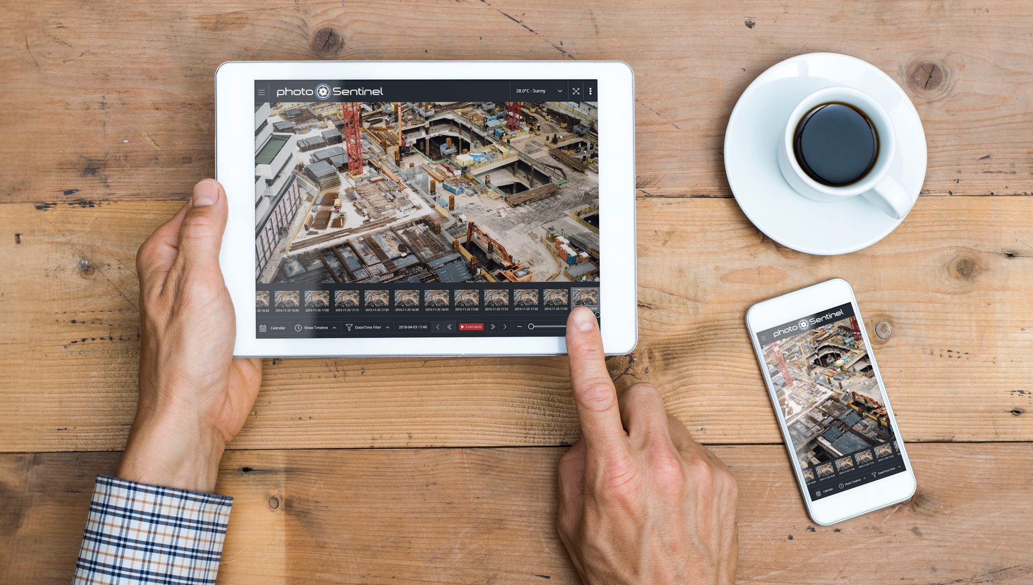 ipad being held by persons hands, with phone and coffee on brown wood table