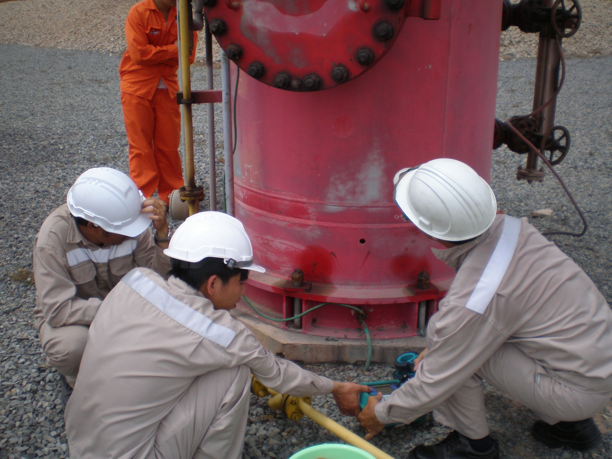 three people in white with white hard hats around a red tall cylinder 